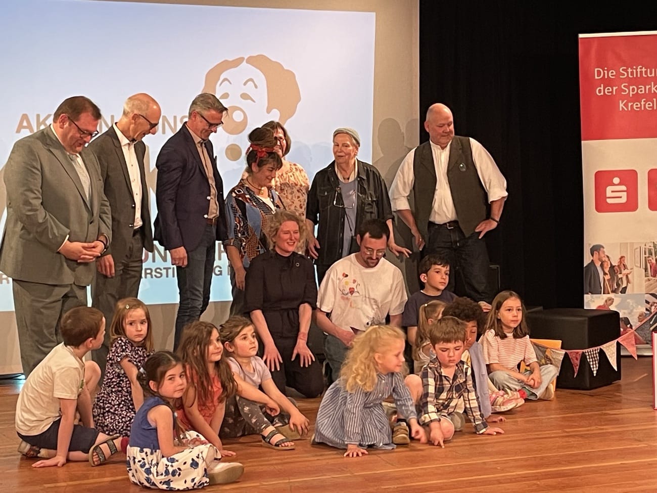 v.l. Hr. Schramm, Sparkassenstiftung; Oberbürgermeister Meyer; Hr. Rausch, Bürgerstiftung; Fr. Doumbaki, Heilpädagogin; Fr. Bambeck, Kita-Leitung; Fr. Schremmer u. Hr. Jansen, AKKU; davor Künstlerin Julia Timmer; Hr. Seeger, Moderation; die preistragenden Kinder